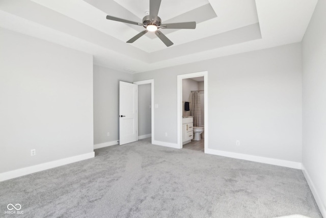 unfurnished bedroom featuring baseboards, a tray ceiling, ensuite bathroom, and light colored carpet