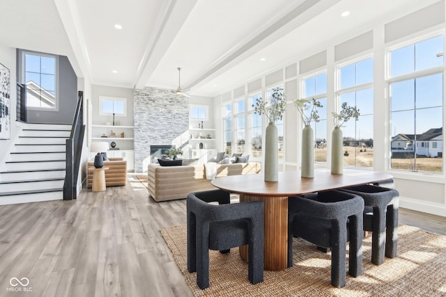 dining area featuring a stone fireplace, recessed lighting, stairway, light wood-type flooring, and beam ceiling