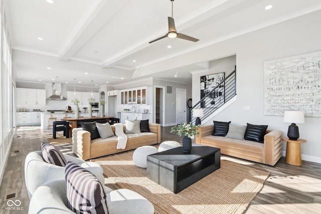 living area featuring light wood-style flooring, beam ceiling, crown molding, and stairway