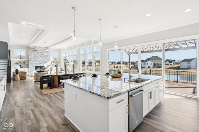 kitchen featuring light stone counters, hanging light fixtures, white cabinets, a sink, and an island with sink