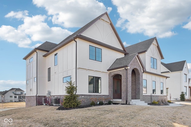 view of front of property featuring cooling unit, brick siding, a shingled roof, a front lawn, and board and batten siding