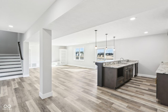 kitchen with a sink, open floor plan, dark brown cabinets, light wood-type flooring, and light stone countertops