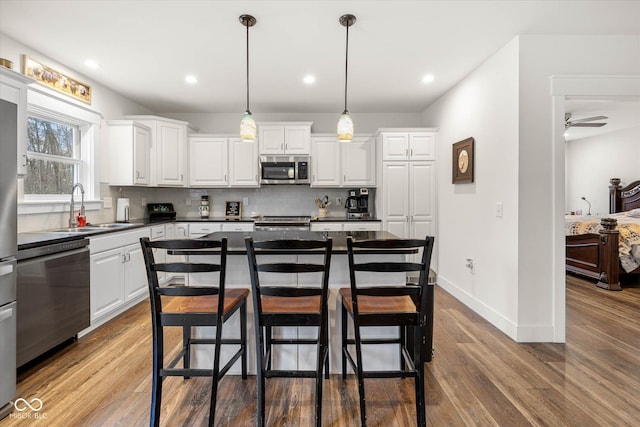 kitchen with dark countertops, a sink, stainless steel appliances, white cabinetry, and backsplash