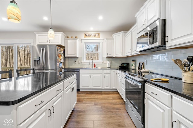 kitchen with white cabinets, appliances with stainless steel finishes, a sink, light wood-style floors, and backsplash