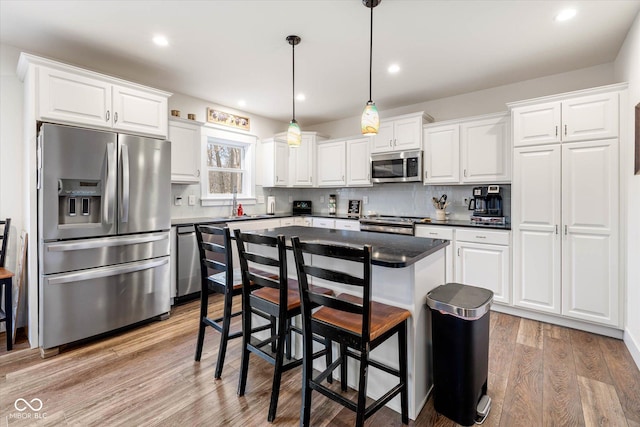 kitchen featuring stainless steel appliances, dark countertops, decorative backsplash, light wood-style floors, and a sink