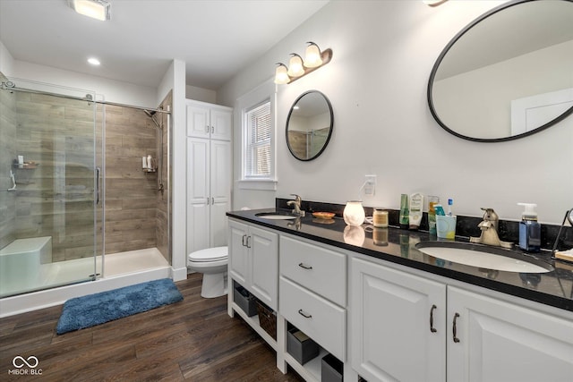 full bathroom with double vanity, a shower stall, a sink, and wood finished floors