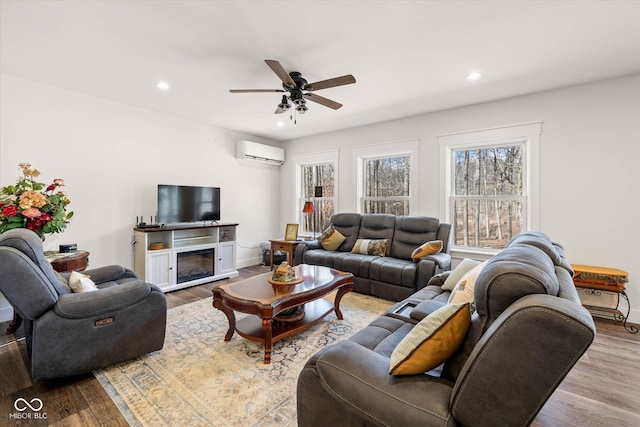 living room with a wall unit AC, recessed lighting, a ceiling fan, a glass covered fireplace, and wood finished floors