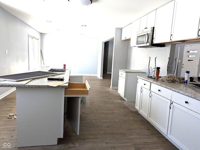 kitchen with baseboards, dark wood finished floors, stainless steel microwave, a center island, and white cabinetry