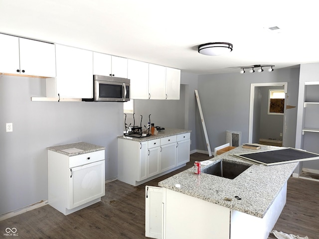 kitchen featuring dark wood-style flooring, stainless steel microwave, a kitchen island with sink, and white cabinets