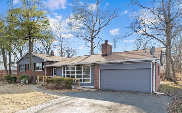 tri-level home with a chimney, aphalt driveway, roof with shingles, an attached garage, and brick siding