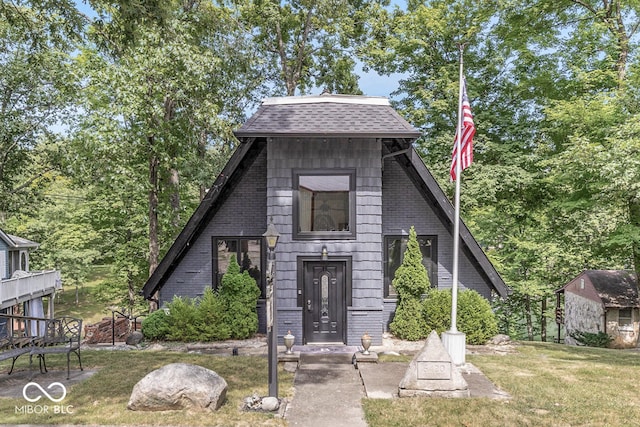 a-frame style home featuring brick siding, roof with shingles, and a front yard