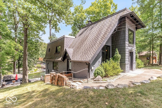 view of side of property with brick siding, a lawn, and roof with shingles