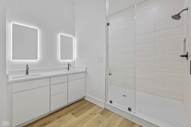 bathroom with double vanity, tiled shower, a sink, and wood finished floors