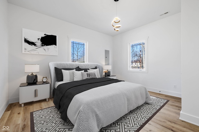 bedroom with multiple windows, light wood-type flooring, and baseboards