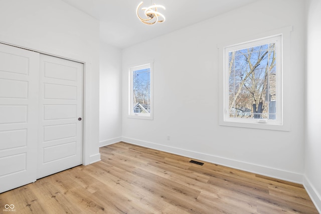 unfurnished bedroom featuring baseboards, visible vents, light wood-type flooring, a chandelier, and a closet