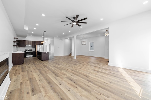 unfurnished living room featuring recessed lighting, stairway, light wood-style floors, a sink, and ceiling fan