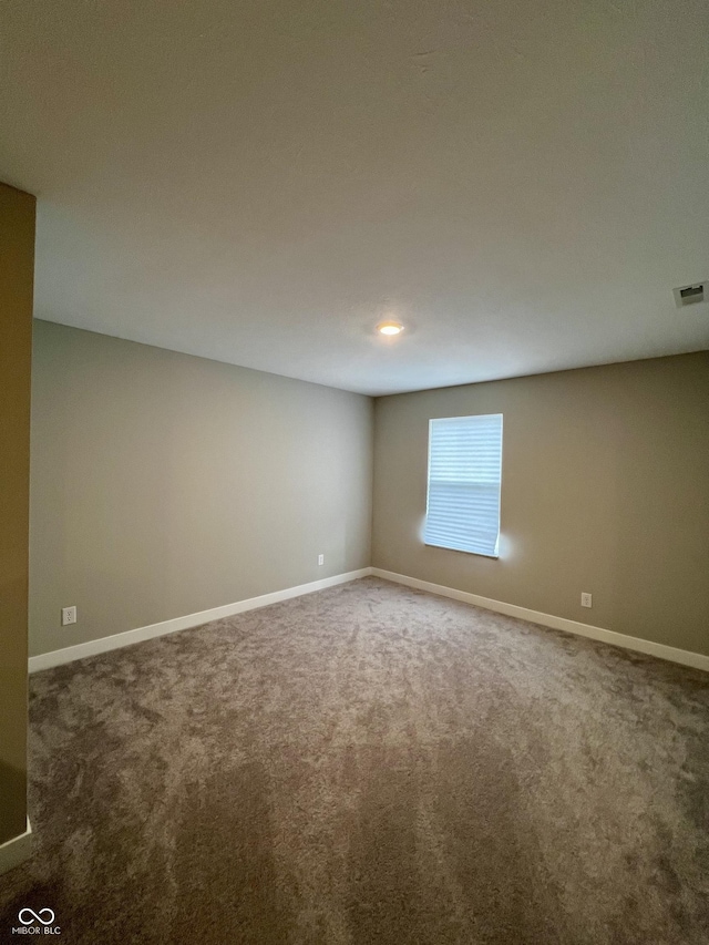 empty room with visible vents, dark carpet, and baseboards