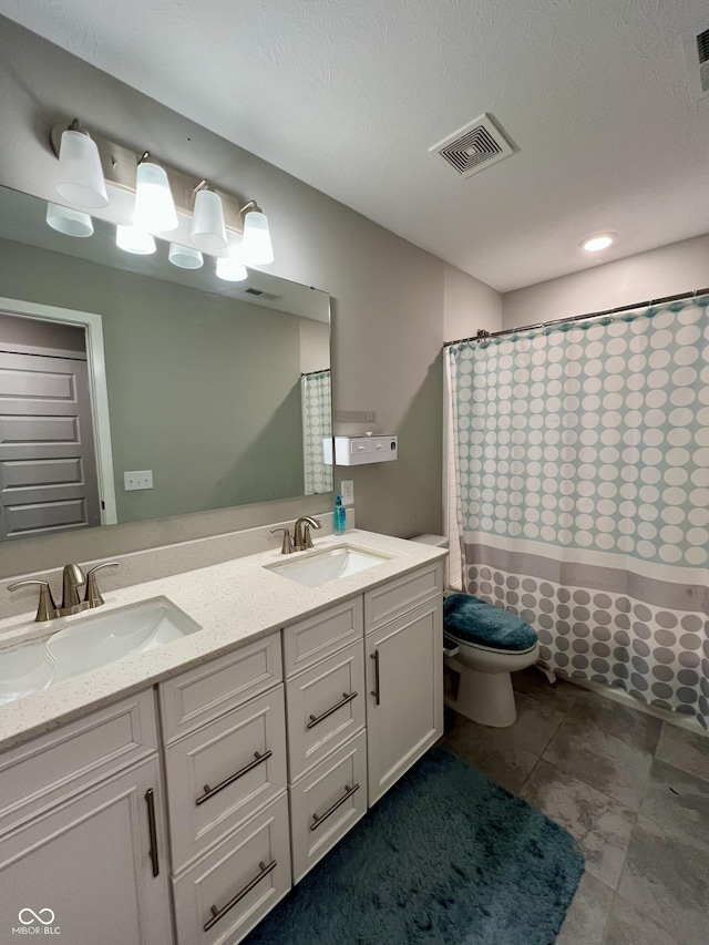 bathroom with double vanity, visible vents, toilet, and a sink