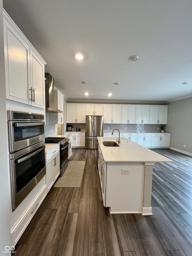 kitchen with stainless steel appliances, a sink, white cabinetry, wall chimney exhaust hood, and an island with sink