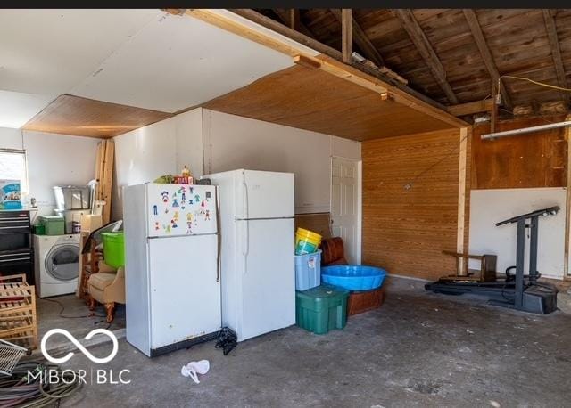 kitchen featuring washer / dryer, wooden walls, unfinished concrete floors, and freestanding refrigerator