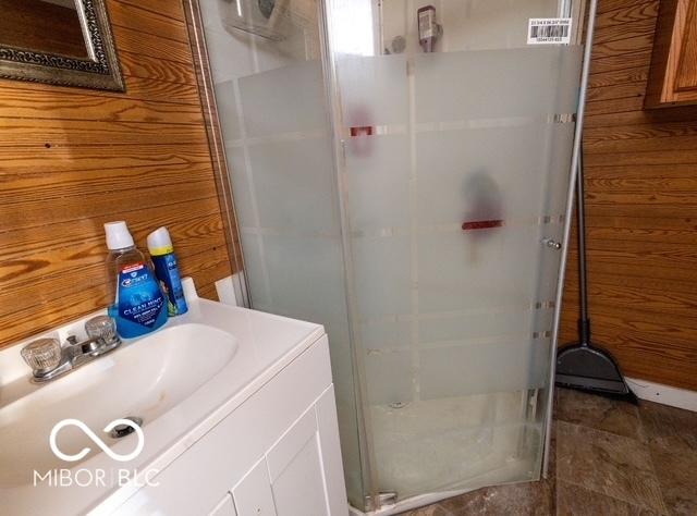 bathroom with wood walls, a shower stall, and vanity