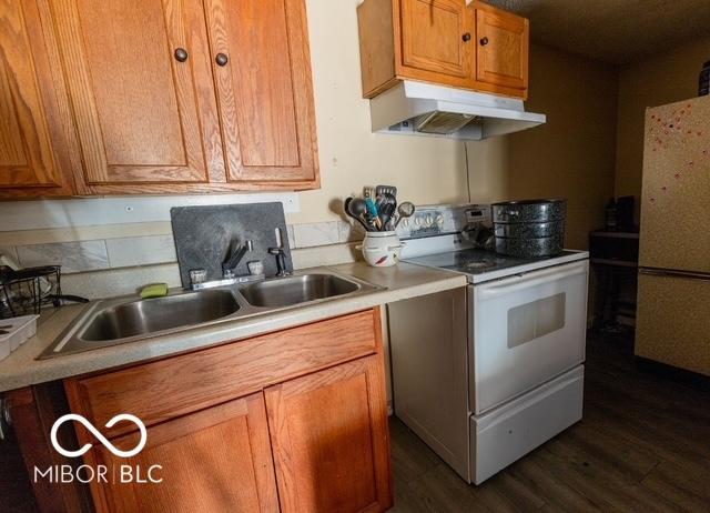 kitchen featuring white appliances, under cabinet range hood, light countertops, and brown cabinetry