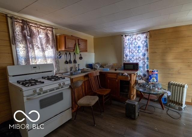 kitchen with light countertops, radiator heating unit, brown cabinetry, wood finished floors, and white gas range oven