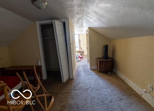 additional living space featuring carpet floors, lofted ceiling, a textured wall, a textured ceiling, and baseboards