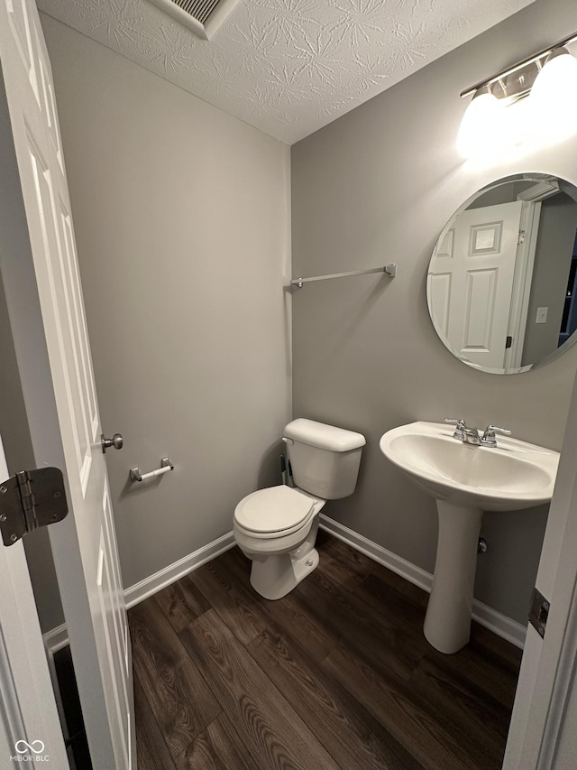 bathroom with visible vents, toilet, a textured ceiling, wood finished floors, and baseboards