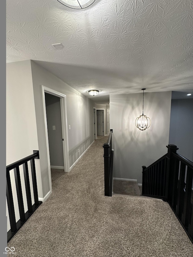 hall featuring baseboards, carpet flooring, a textured ceiling, and an upstairs landing