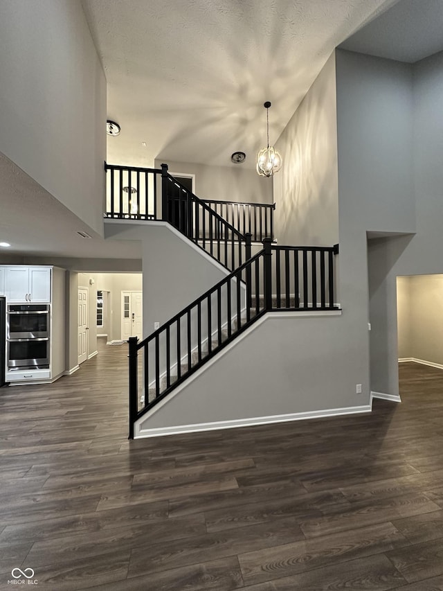 staircase with a notable chandelier, a high ceiling, baseboards, and wood finished floors