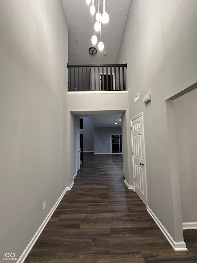 hall featuring a towering ceiling, a textured ceiling, baseboards, and dark wood-style flooring