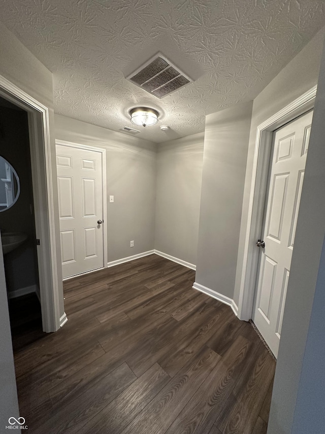 empty room with visible vents, dark wood finished floors, a textured ceiling, and baseboards