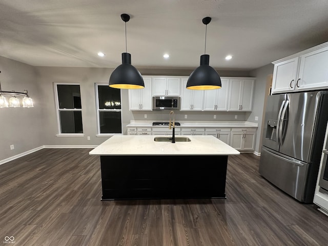 kitchen with hanging light fixtures, appliances with stainless steel finishes, a center island with sink, and white cabinetry