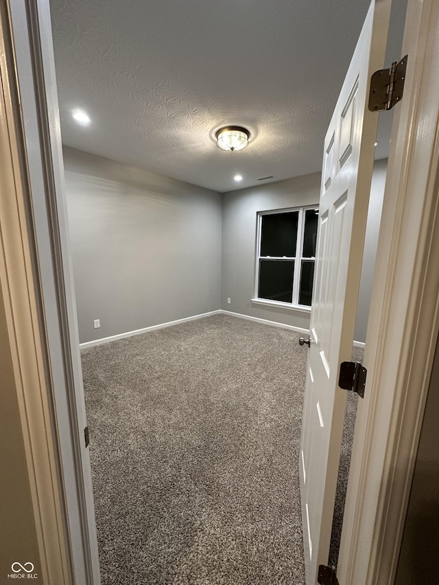 carpeted spare room with a textured ceiling and baseboards