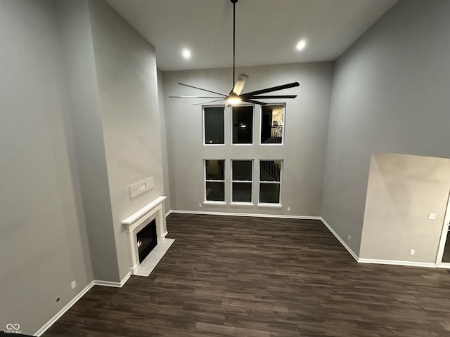 unfurnished living room with ceiling fan, dark wood-type flooring, a fireplace with flush hearth, and baseboards