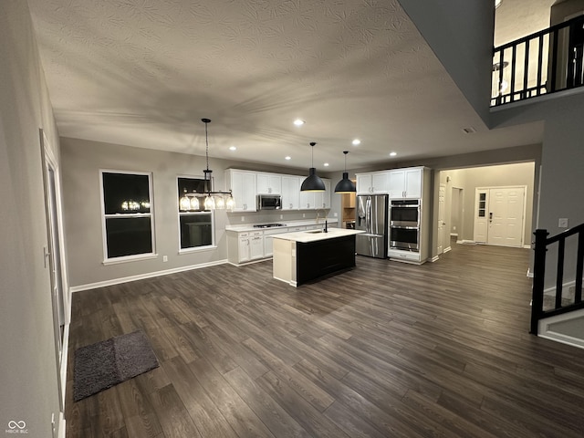 kitchen with pendant lighting, light countertops, appliances with stainless steel finishes, a kitchen island with sink, and white cabinets