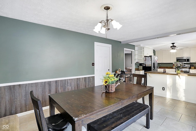 dining room featuring a wainscoted wall, wooden walls, a textured ceiling, and ceiling fan with notable chandelier