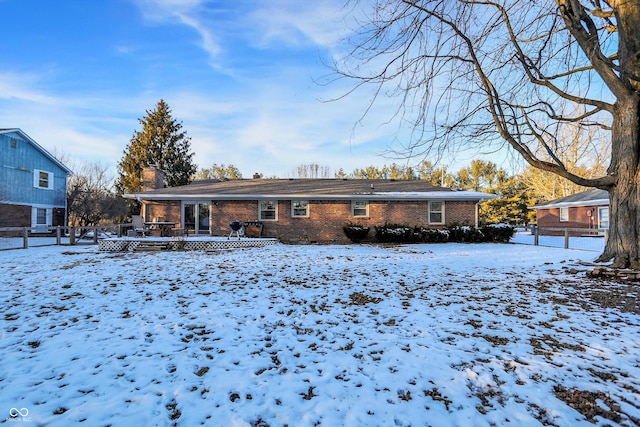 snow covered property featuring brick siding, fence, and a chimney