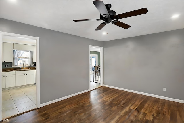 empty room with ceiling fan, a sink, baseboards, and wood finished floors