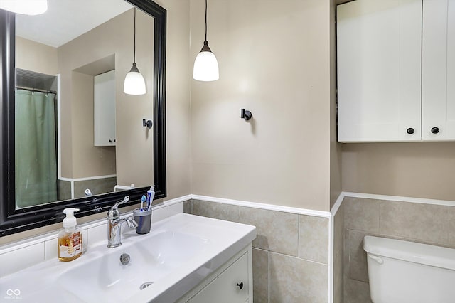 bathroom with tile walls, a wainscoted wall, vanity, and toilet