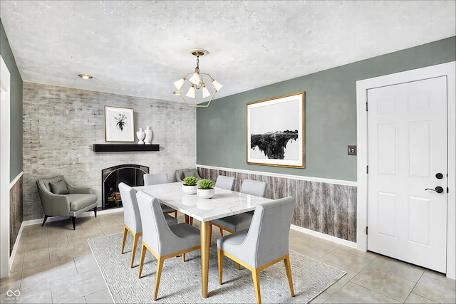 dining area with light tile patterned floors, a wainscoted wall, a fireplace, and an inviting chandelier