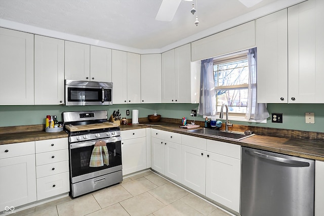 kitchen with light tile patterned floors, stainless steel appliances, white cabinetry, wooden counters, and a sink