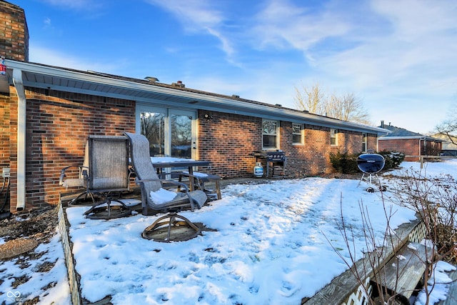 snow covered back of property featuring a chimney and brick siding