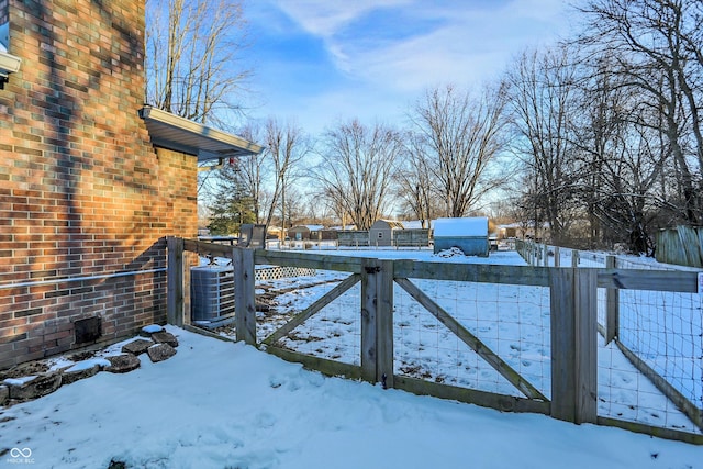 snowy yard with central AC, fence, and a gate