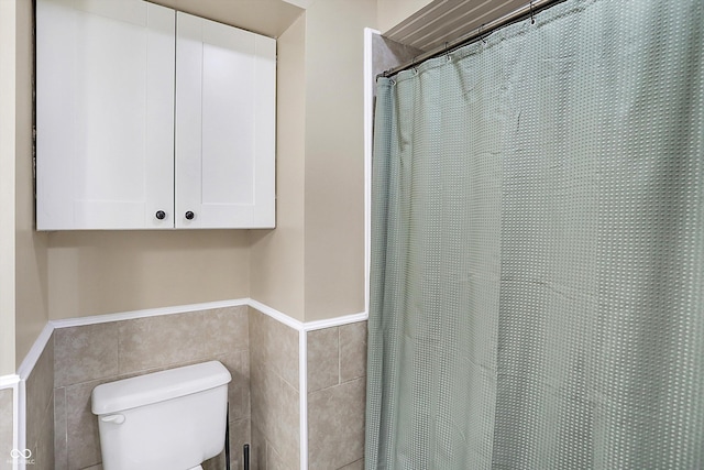 bathroom featuring toilet, wainscoting, tile walls, and a shower with shower curtain