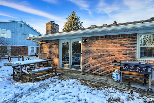 snow covered property featuring brick siding and a chimney