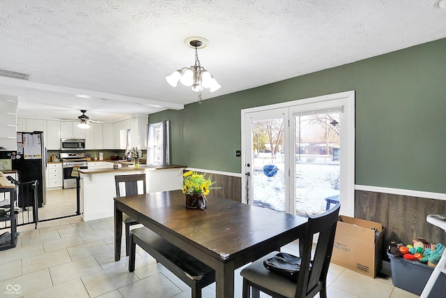 dining space featuring light tile patterned floors, a textured ceiling, wooden walls, a wainscoted wall, and visible vents