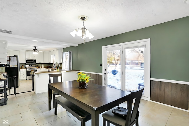 dining area featuring light tile patterned floors, visible vents, wainscoting, a textured ceiling, and a notable chandelier