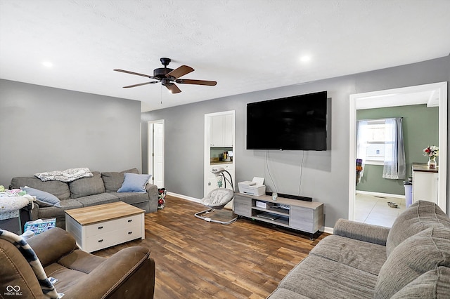 living area featuring ceiling fan, baseboards, and dark wood-type flooring